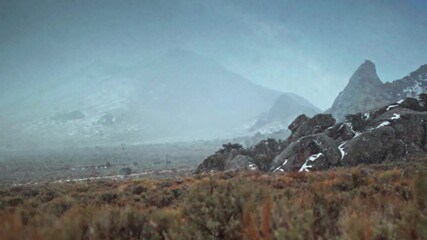 Panning shot across mountains obscured by a snowstorm and pull focus to desert sagebrush in Castle Rocks State Park, Idaho