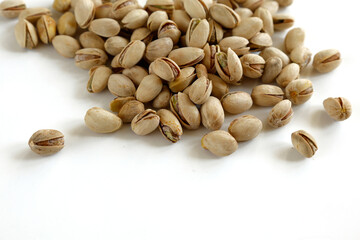 A scattered pile of unshelled pistachios lies on a clean white background, emphasizing the natural texture and details of the nuts. 