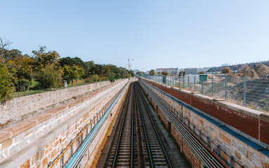 Empty train tracks stretching into the distance, bordered by stone walls and flanked by a construction site and a park in vienna, austria, on a clear day