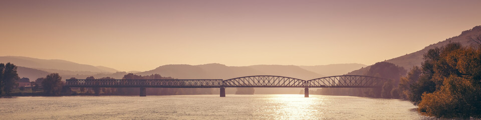Long railway bridge crossing the danube river at sunset in krems an der donau, austria, with hills and trees in the background, creating a beautiful and peaceful landscape