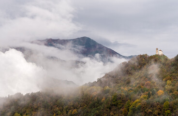 Suggestive Mountain Landscape with Fog and Sunbeams. Ancient Lonely Church on the Top of the Mountain, autumn colors.
