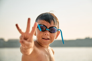 Fototapeta premium A small boy wearing swim goggles plays at the waters edge and jumps into the water