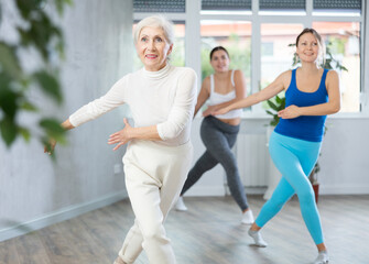 Obraz premium Energetic women of different ages warming up with dancing elements before training together in fitness center