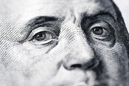 Close-up macro photograph with soft focus of Benjamin Franklin&rsquo;s eyes on a U.S. one-hundred-dollar bill, detailed textures and intricate patterns of fine lines and dots. Design of the currency.