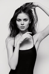 Fototapeta premium Elegant young woman with long hair in black bodysuit, expressing confidence and strength with her hand in her hair. Studio shot on white background.