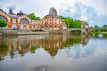 Fototapeta premium The picturesque Art Nouveau hydroelectric power station stands by the calm river in Hradec Kralove, Czechia, reflecting its unique architectural beauty against the serene water and surrounding