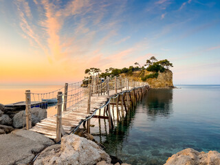 Obraz premium A wooden bridge leads to a small island in the calm sea at sunset