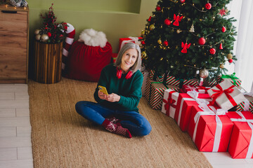 Photo of lovely elderly woman sit floor wear green pullover enjoy new year preparation christmas cozy atmosphere indoors home