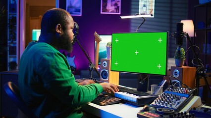 Musician operates on midi controller piano keys next to mockup screen, producing new songs with...
