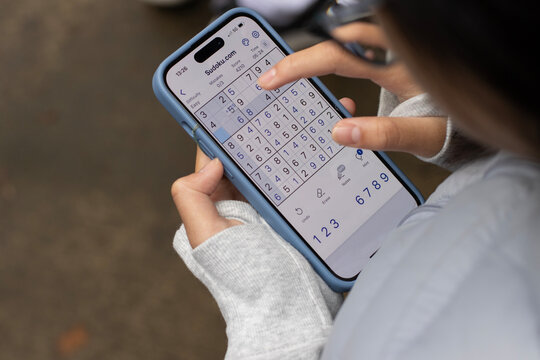 Portland, OR, USA - Nov 3, 2024: A girl plays Sudoku puzzle game on an iPhone. Sudoku is a logic-based, combinatorial number-placement puzzle.