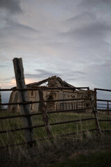 old abandoned dovecote with a partially collapsed roof, set against a dramatic evening sky. The surrounding grass and distant buildings add a rural charm, highlighting the beauty of decay and solitude