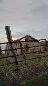 old abandoned dovecote with a partially collapsed roof, set against a dramatic evening sky. The surrounding grass and distant buildings add a rural charm, highlighting the beauty of decay and solitude