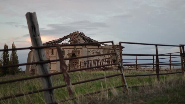 old abandoned dovecote with a partially collapsed roof, set against a dramatic evening sky. The surrounding grass and distant buildings add a rural charm, highlighting the beauty of decay and solitude