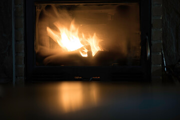 Cozy close-up of a burning fireplace casting warm, flickering light in a dark room. The soft reflections of the firelight create a comforting ambiance, perfect for themes of warmth and winter nights.