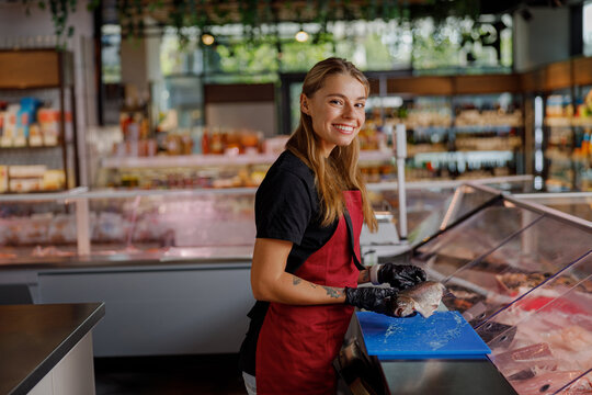 A cheerful and dedicated worker happily serves fresh, quality meats in a bustling and lively grocery store deli
