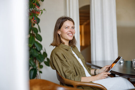 A cheerful woman relaxing with a tablet in a stylish caf surrounded by greenery