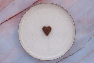 Heart-shaped chocolate on ceramic plate with marble background