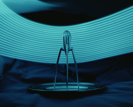 There is a Juicy Salif citrus juicer that is currently resting on a plate while illuminated by a blue light positioned behind it, creating an interesting visual lemon juicer