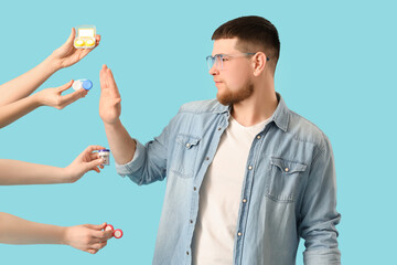 Young man in eyeglasses rejecting contact lenses on blue background