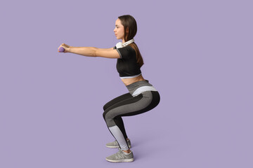 Young female trainer with headphones and dumbbells doing exercise on lilac background