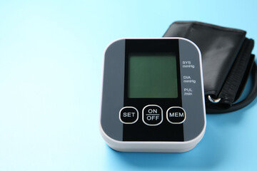 Blood pressure measuring device on light blue background, closeup. Space for text