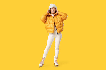 Happy young Asian woman in ice skates on yellow background