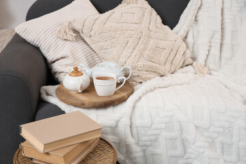 Teapot and cup of tea with books on sofa in room