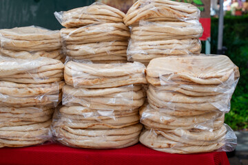 Multiple bags of corn tortilla wraps, gluten-free, for sale at a farmer's market. The Mexican food is a light beige color and is in bags with a count of ten. The cooked wraps are small and round.