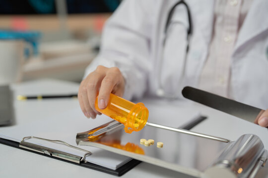 Doctor carefully pouring pills from orange bottle onto metal tray in pharmacy setting, highlighting importance of accuracy in medication preparation