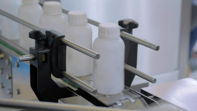 Production line, conveyor belt of bottle shrink sleeve labeling machine with empty white plastic bottles at packaging exhibition or factory: demonstration mode - close up view