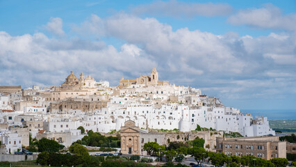 Naklejka premium Nestled atop a hill, Ostuni showcases its enchanting whitewashed buildings against a backdrop of blue skies , inviting visitors to explore its captivating streets and rich history of Italy