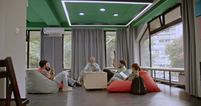 A group of students sits comfortably in beanbag chairs at the library, engaging in a lively discussion with their professor as they collaborate on their studies.