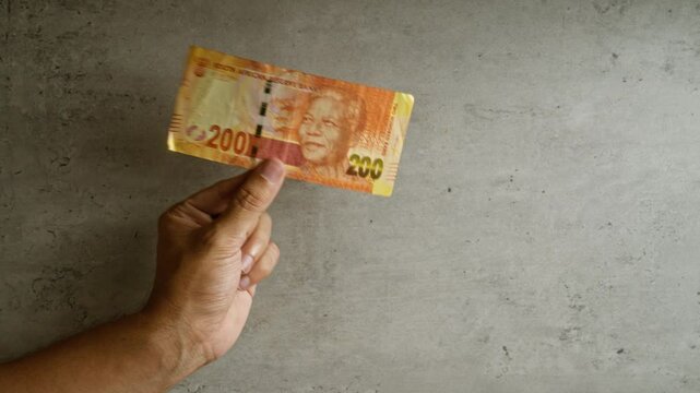 Man holding 200 rands south african banknote against a concrete background