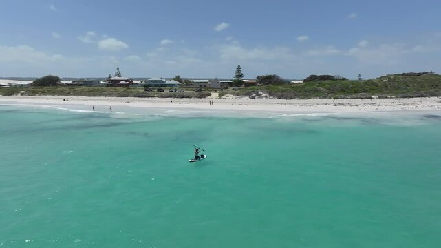 Man returns to shore paddling in to the beach in calm conditions with perfect blue water.