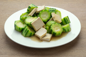 close up view of stir fried luffa with hard tofu in a ceramic dish on wooden table. asian homemade style healthy food concept.