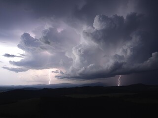 Fototapeta premium Towering thunderclouds with lightning illuminating the darkening landscape, heavy rain clouds, darkening horizon, flash flood