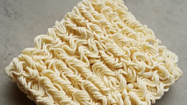Closeup image of uncooked instant noodles on a grey surface with detailed texture showcasing its wavy pattern and dry appearance