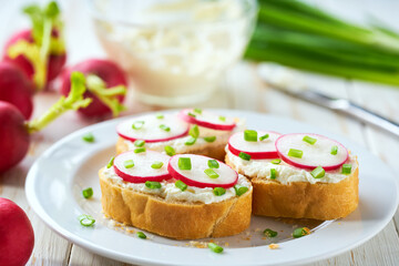 Cutting baguette with soft cream cheese and radish on a light kitchen table. Tasty summer snacks.