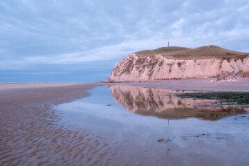 Pastelcolored coastal cliffs are reflected in a calm tidal pool on a sandy beach during a serene evening