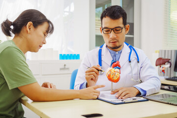 A doctor man sits at a desk in a hospital, explaining heart disease symptoms to a female patient. They discuss chest pain, palpitations, fatigue, dizziness, and the risks of myocardial ischemia