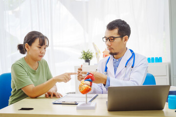 Fototapeta premium A doctor man sits at a desk in a hospital, explaining heart disease symptoms to a female patient. They discuss chest pain, palpitations, fatigue, dizziness, and the risks of myocardial ischemia