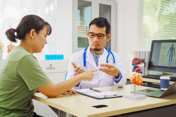A doctor man sits at a desk in a hospital, explaining heart disease symptoms to a female patient. They discuss chest pain, palpitations, fatigue, dizziness, and the risks of myocardial ischemia