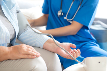 Obraz premium Caregiver young woman measuring blood pressure with patient elderly for checkup pulse health and examining in living room at home, nurse checkup patient for health care, medical and insurance.