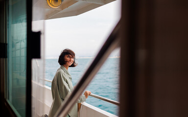A young woman stands on the deck of a cruise ship and smiles. The girl smiles while traveling. A...