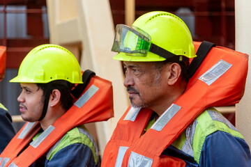 Crew members wear life jackets as they gather for an abandon ship drill, reviewing lifeboat deployment. Their safety gear and focused expressions underscore the critical nature of these exercises.