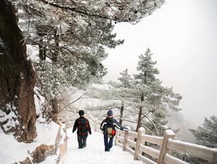 Two backpackers walking down the steps in the snow. Mount Huangshan. Anhui province. China.