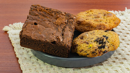  Delicious chocolate brownie and assorted cookies on a plate over a rustic knitted mat, perfect for dessert and snack themes.