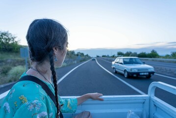 Female hitchhiker rides in the back of a pickup truck on a Turkish highway. © Wirestock
