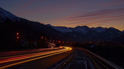 As the sun sets behind the mountains car light trails take over creating a lively atmosphere on the road to the ski resort.