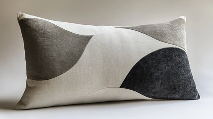 A white rectangular pillow with grey and black geometric shapes on it.